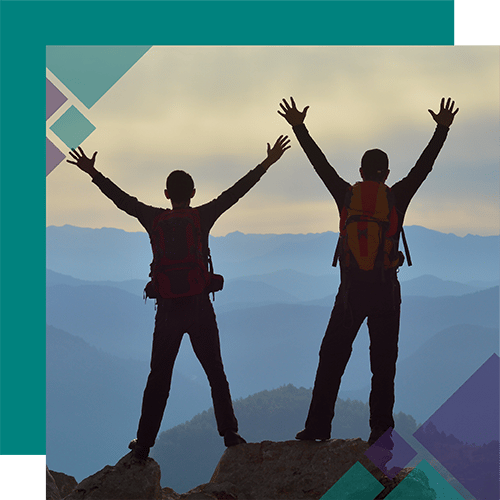 Two men standing at summit of mountain with arms raised in the air